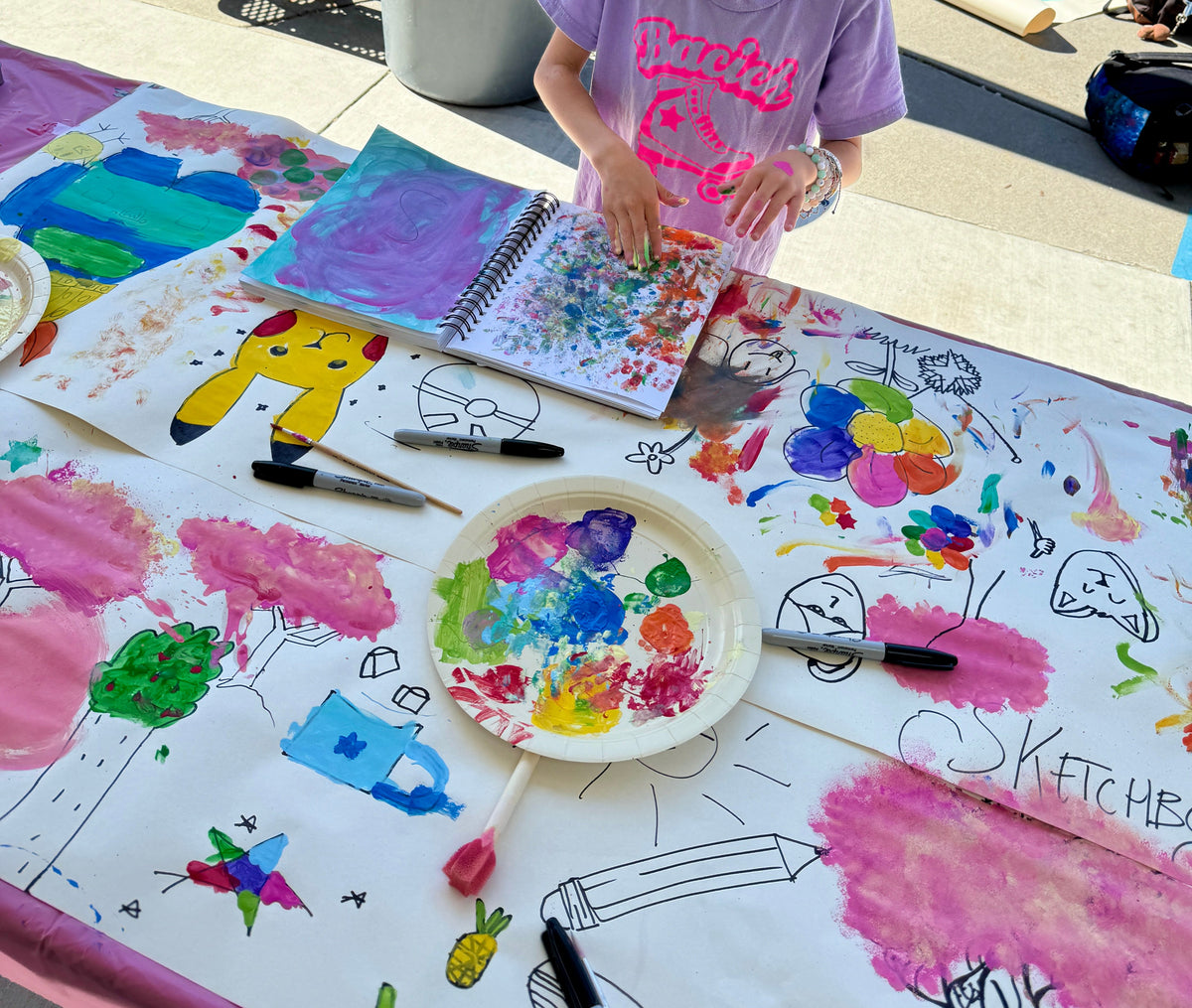 Child painting at a table with art supplies outdoors