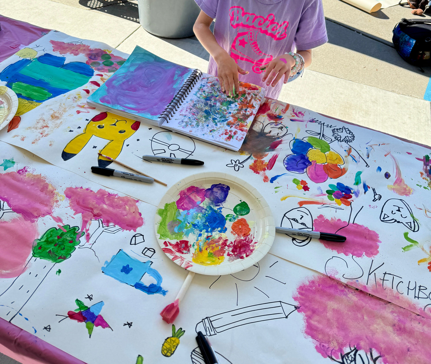 Child painting at a table with art supplies outdoors